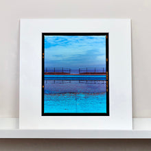 Load image into Gallery viewer, Mounted photograph by Richard Heeps. The blue bay at Llandudno, cut across the middle with path and railings with a gap right in the middle.