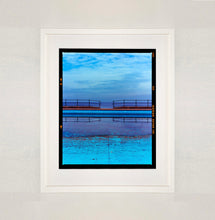 Load image into Gallery viewer, White framed photograph by Richard Heeps. The blue bay at Llandudno, cut across the middle with path and railings with a gap right in the middle.