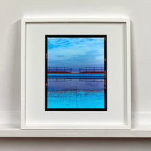 Load image into Gallery viewer, White framed photograph by Richard Heeps. The blue bay at Llandudno, cut across the middle with path and railings with a gap right in the middle.