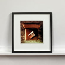 Load image into Gallery viewer, Black framed photograph by Richard Heeps. The photograph looks down on a brown padded side chair. On it sits a waterstained and battered brown covered Holy Bible.