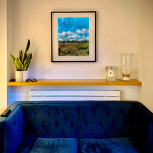 Load image into Gallery viewer, Black framed photograph by Richard Heeps in situ. Feathers, leaves, sticks and other fenland debris appears at the front of this photograph with a hazy blue fenland sky and scene blurred behind.