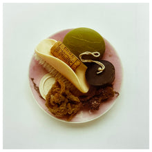 Load image into Gallery viewer, Photograph by Richard Heeps. A vintage pink soap dish sits on a white surface. Looking down onto the soap dish which contains two plugs, green soap, nail brush, cork and a sponge/wire wool combo.
