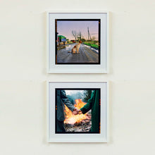 Load image into Gallery viewer, Two white framed photographs by Richard Heeps. The top photograph features a brown and white patched/speckled dog sitting in the middle of Fenland road. Farmers trucks and vehicles are strewn next to the road on the right hand side. The bottom photographs is in a forest - hands are held with arms dressed in retro green clothing, behind roars a fire.