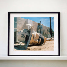 Load image into Gallery viewer, Black framed photograph by Richard Heeps. The broken off head of a giant fibreglass sculpture of a cowboy (a Muffler Man) lies on the ground.