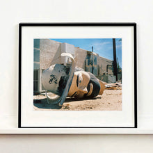 Load image into Gallery viewer, Black framed photograph by Richard Heeps. The broken off head of a giant fibreglass sculpture of a cowboy (a Muffler Man) lies on the ground.