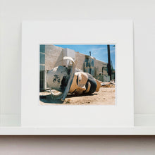 Load image into Gallery viewer, Mounted photograph by Richard Heeps. The broken off head of a giant fibreglass sculpture of a cowboy (a Muffler Man) lies on the ground.