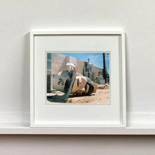 Load image into Gallery viewer, White framed photograph by Richard Heeps. The broken off head of a giant fibreglass sculpture of a cowboy (a Muffler Man) lies on the ground.