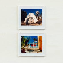 Load image into Gallery viewer, Two white framed photographs by Richard Heeps. The the top photograph, in the foreground of the photograph is a broken off head of a giant fibreglass sculpture of a cowboy (a Muffler Man). In the background set in a deep blue sky is the muffler man's headless torso. The bottom photograph shows a colourful Californian motel against a blue sky.
