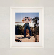 Load image into Gallery viewer, White framed photograph by Richard Heeps. The headless torso of a giant fibreglass sculpture of a cowboy (a Muffler Man).