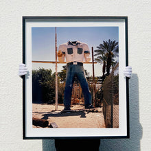 Load image into Gallery viewer, Black framed photograph held by photographer Richard Heeps. The headless torso of a giant fibreglass sculpture of a cowboy (a Muffler Man).