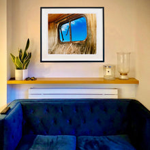 Load image into Gallery viewer, In situ black framed photograph by Richard Heeps. The interior of an eroded trailer, looking through the broken window to a deep blue sky.