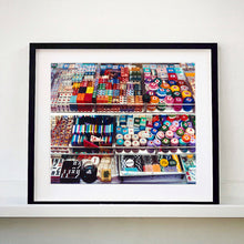 Load image into Gallery viewer, Black framed photograph by Richard Heeps. Three compartmentalised shop shelves, each compartment has coloured plastic dice, counters, circular containers, cards, poker chips, and other plastic type games items.