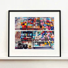 Load image into Gallery viewer, Black framed photograph by Richard Heeps. Three compartmentalised shop shelves, each compartment has coloured plastic dice, counters, circular containers, cards, poker chips, and other plastic type games items.
