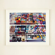 Load image into Gallery viewer, White framed photograph by Richard Heeps. Three compartmentalised shop shelves, each compartment has coloured plastic dice, counters, circular containers, cards, poker chips, and other plastic type games items.