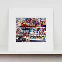 Load image into Gallery viewer, Mounted photograph by Richard Heeps. Three compartmentalised shop shelves, each compartment has coloured plastic dice, counters, circular containers, cards, poker chips, and other plastic type games items.
