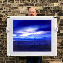 Load image into Gallery viewer, Photograph held by photographer Richard Heeps. A blue light hits vast land, mountains and a big sky.