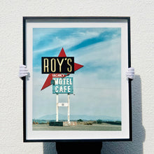 Load image into Gallery viewer, Photograph held by photographer Richard Heeps. A roadside sign on Route 66 in America. The word ROY'S appears in a black sign with a big red arrow pointing to the left ground, below this VACANCY and on a green square the words MOTEL and CAFE.
