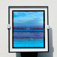 Load image into Gallery viewer, Photograph held by photographer Richard Heeps. The blue bay at Llandudno, cut across the middle with path and railings with a gap right in the middle.
