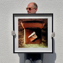 Load image into Gallery viewer, Black framed photograph held by photographer Richard Heeps. The photograph looks down on a brown padded side chair. On it sits a waterstained and battered brown covered Holy Bible.