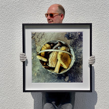 Load image into Gallery viewer, Black framed photograph held by photographer Richard Heeps. A bucket with sponges, brushes and wooden handled tools sit in a bucket on a cracked cement floor.