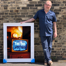 Load image into Gallery viewer, Photograph held by photographer Richard Heeps. A retro small brown television sits on a wooden table displaying The End on a black and white film which shows as blue and white. In the background of the television is a warm light.