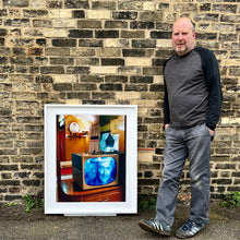 Load image into Gallery viewer, White framed photograph with photographer, Richard Heeps. A retro small brown television sits on a wooden table displaying a black and white film, with the face of Clark Gable filling the screen, it shows as blue and white. In the background of the television is a warm wood-panelled light.