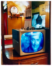 Load image into Gallery viewer, Photograph by Richard Heeps. A retro small brown television sits on a wooden table displaying a black and white film, with the face of Clark Gable filling the screen, it shows as blue and white. In the background of the television is a warm wood-panelled light.