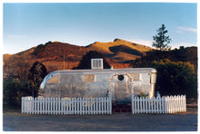 Load image into Gallery viewer, This artwork brings about a romantic dream of living in an RV. Captured in the morning sun at the start of a beautiful Arizona day, this RV is surrounded by both a white picket fence and a beautiful landscape, with the sun tickling the hilltops. Photographed as part of Richard Heeps&#39; &#39;Dream in Colour&#39; series.
