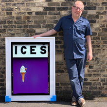 Load image into Gallery viewer, Photograph by Richard Heeps.  Richard Heeps holds a white framed print. At the top of the print, black letters spell out ICES and below is depicted a 99 icecream cone sitting left of centre against a purple coloured background.  