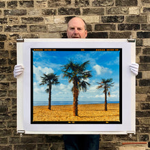 Load image into Gallery viewer, Photograph held by photographer Richard Heeps.  Three palm trees on the beach at Clacton-on-Sea with shadows cast by the early evening light.