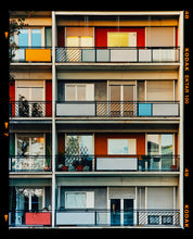 Load image into Gallery viewer, Photograph by Richard Heeps. This is the balconies and balcony doors of 4 floors of flats located on the Rue Dezza. The colours of the walls alternate between red and grey but look different as the light catches them.