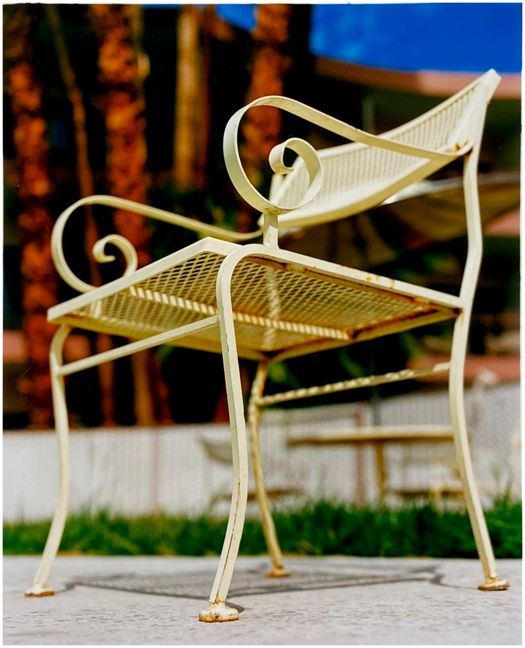 Photograph by Richard Heeps. A cream chair sits on hard standing, behind the chair and slightly out of focus is lush green grass and warm red tree trunks.