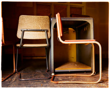 Load image into Gallery viewer, Photograph by Richard Heeps.  Two metal framed chairs with padded seats and backs. On the left hand side of the photo is one of the chairs facing backwards, on the right handside is a chair facing right. The chairs sit next to a metal cabinet. The floor is covered in small shavings of debris.