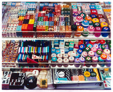 Load image into Gallery viewer, Photograph by Richard Heeps. Three compartmentalised shop shelves, each compartment has coloured plastic dice, counters, circular containers, cards, poker chips, and other plastic type games items.