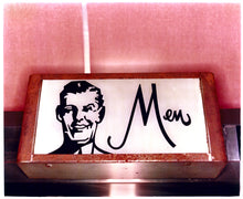 Load image into Gallery viewer, Photograph by Richard Heeps. A kitsch Men&#39;s toilet sign. The sign has the word Men alongside an outline of 1950s man. The sign sits in a wooden frame and sits against a pink tiled wall.