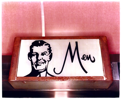 Photograph by Richard Heeps. A kitsch Men's toilet sign. The sign has the word Men alongside an outline of 1950s man. The sign sits in a wooden frame and sits against a pink tiled wall.