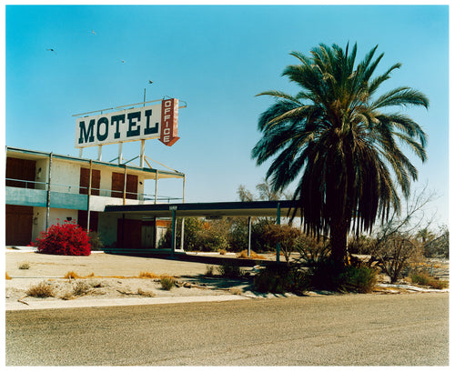 Photograph by Richard Heeps. A derelict motel office sits on a dusty American road. A large palm tree sits at the front of the office's walkway.