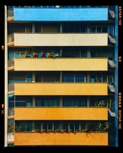 Load image into Gallery viewer, Photograph by Richard Heeps. Photograph of an apartment building with coloured balconies, blue at the top balcony and then fading from light yellow to a sunburnt yellow at the bottom.