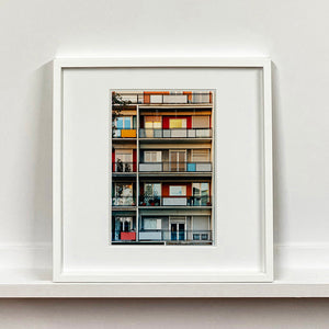 White framed photograph by Richard Heeps. A colourful set of walls and balconies over five floors.