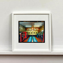 Load image into Gallery viewer, White framed photograph by Richard Heeps. A laundrette with washing machines on each wall and a double sided seat in the middle.