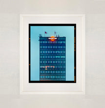 Load image into Gallery viewer, White framed photograph by Richard Heeps. High rise offices in a blue light with Martini logo on the top facade. 