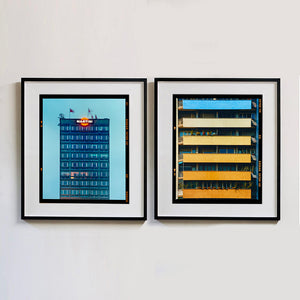 Two black framed photographs by Richard Heeps. On the left hand side is a photograph of high rise offices in a blue light with Martini logo on the top facade. The photo on the right hand side is of 5 floor flat with blocks of colour on each balcony, the top one blue and then light yellow fading up to a darker yellow at the bottom.