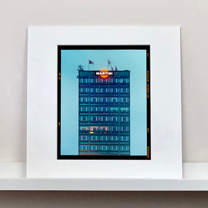 Mounted photograph by Richard Heeps. High rise offices in a blue light with Martini logo on the top facade. 