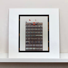 Load image into Gallery viewer, White mounted photograph by Richard Heeps. High rise offices with Martini logo on the top facade. 