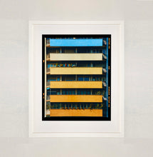 Load image into Gallery viewer, White framed photograph by Richard Heeps. Photograph of an apartment building with coloured balconies, blue at the top balcony and then fading from light yellow to a sunburnt yellow at the bottom.