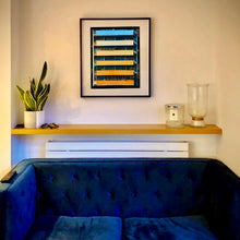 Load image into Gallery viewer, In situ black framed photograph by Richard Heeps. Photograph of an apartment building with coloured balconies, blue at the top balcony and then fading from light yellow to a sunburnt yellow at the bottom.