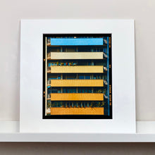 Load image into Gallery viewer, Mounted photograph by Richard Heeps. Photograph of an apartment building with coloured balconies, blue at the top balcony and then fading from light yellow to a sunburnt yellow at the bottom.