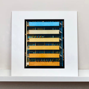 Mounted photograph by Richard Heeps. Photograph of an apartment building with coloured balconies, blue at the top balcony and then fading from light yellow to a sunburnt yellow at the bottom.