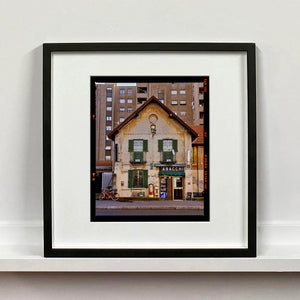Black framed photograph by Richard Heeps. A traditional Italian Tobacconist shop, here in a Swiss Cottage style building set against a vast urban apartment block.
