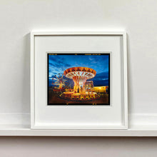 Load image into Gallery viewer, White framed photograph by Richard Heeps. A fairground ride, the chairoplanes, sits lit in golden and red colours against a dark blue sky.